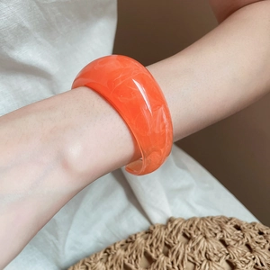 Detail view of orange resin bangle with white marble texture on a female model