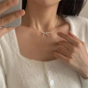 Detailed view of an elegant pearl bow pendant on a gold chain worn on the collarbone