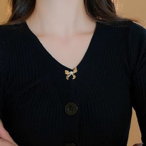 Detailed view of a gold bow brooch with pearl on a black knit sweater neckline