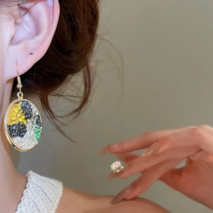 Detailed close-up of a gold oval earring with colorful inlaid stones worn on the ear