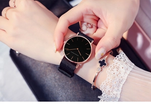 Close-up of elegant black dial watch with rose gold case and nylon strap worn with jewelry