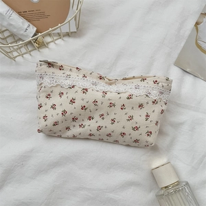 Close-up of floral makeup bag with red roses, lace trim, and zipper closure on soft fabric