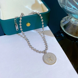 Close-up of silver steel beaded bracelet with Queen Elizabeth coin pendant on a jewelry box