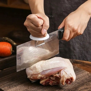 Macro shot of a stainless steel kitchen knife slicing raw chicken on a wooden board