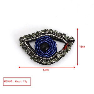 Macro detail of embroidered evil eye brooch with blue beads and crystals, 63mm by 43mm