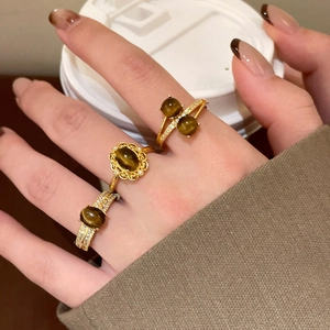 Dettaglio di anelli placcati oro con occhio di tigre e zirconi su maglione autunnale