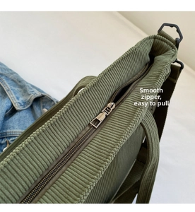 Detail of the smooth dark grey metal zipper closure on a green corduroy tote bag