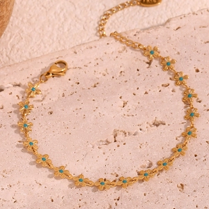 Detail of 18K gold-plated flower bracelet with blue enamel centers on stone background