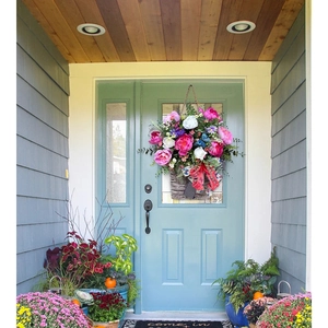 Close-up of artificial floral basket with pink peonies and bow on a blue front door