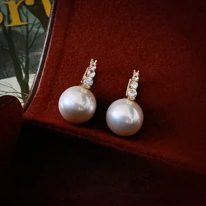 Elegante vergoldete Perlenohrringe mit Zirkoniasteinen auf Vintage Samthintergrund