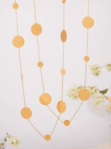 Gros plan de colliers dorés avec pendentifs circulaires suspendus devant un mur naturel