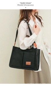 Detail of black canvas tote bag showing outer pockets and brown leather trim accents