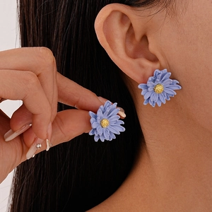Detailed close-up of a blue daisy earring with golden stamen worn on a model ear