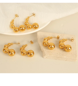 Detail view of gold sphere drop earrings with mirror finish on natural stone background