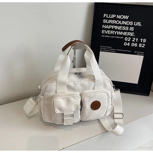 Detail der weißen Canvas-Tasche mit braunem Logo-Abzeichen und zwei vorderen Utensilientaschen