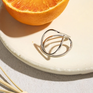 Minimalist wave cross ring in silver steel finish displayed on a ceramic plate