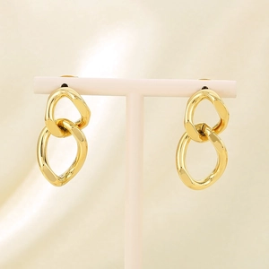 Detail of gold double-link twist earrings displayed on a white stand over beige silk