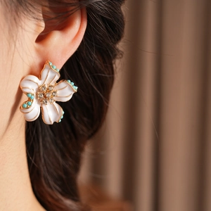 Gros plan de boucles d'oreilles fleur vintage en émail blanc et perles turquoise