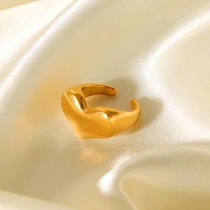 Macro shot of a polished golden heart-shaped open ring on a luxury cream silk background