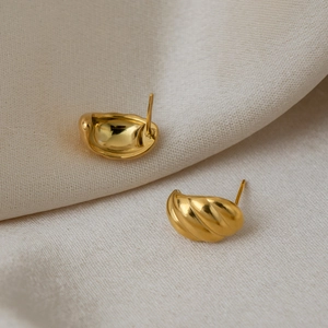 Close-up of 18K gold plated C-shape earrings with striped texture on beige silk fabric