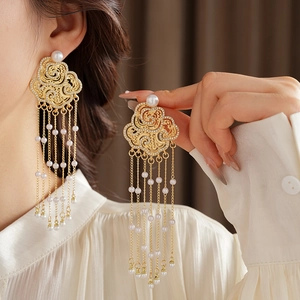 Detailed view of gold tassel earrings with cloud pattern and pearls worn by a model