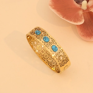 Close-up of vintage gold hollowed cuff bracelet with three inlaid turquoise stones on peach