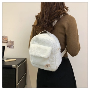 Detalle de mochila blanca de felpa con etiqueta Good Luck mostrada por modelo real