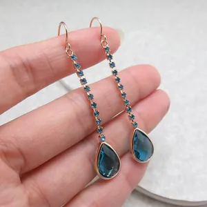 Close-up of long rose gold drop earrings with blue crystals and elegant teardrop pendants