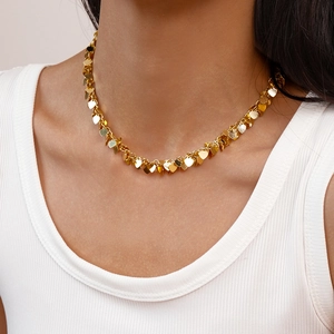 Close-up of a gold sequin heart fringe necklace on a model wearing a white top