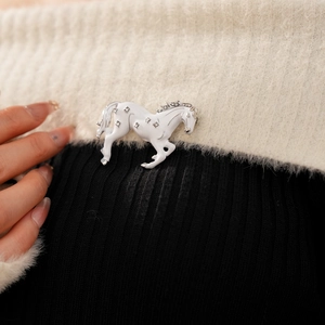 Close-up of a vintage horse brooch with white enamel and rhinestones on a sweater
