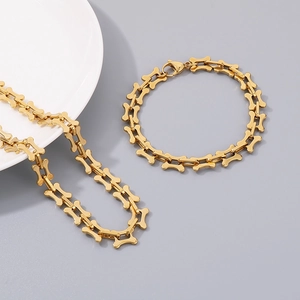 Detailed view of gold bone-shaped chain link necklace and bracelet set on a grey surface