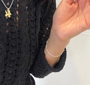 Close-up of a silver twisted chain bracelet and a yellow balloon dog pendant on a model