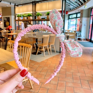 Détail d'un serre-tête floral rose avec un nœud à motif cerise tenu à la main