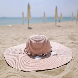 Detail of pink straw sun hat with decorative seashells and beads for beach protection