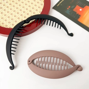 Flat lay of matte black banana clip and khaki oval hair clip on a woven tray decor