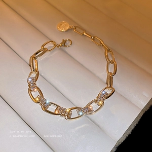 Elegantes Goldkettenarmband mit Zirkonia und Münzanhänger auf beigem Grund