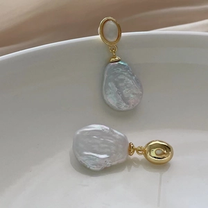 Detailed view of baroque pearl gold earrings displayed on a white ceramic plate