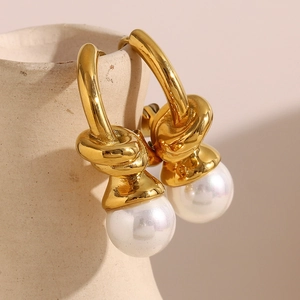 Detail of 18K gold plated knotted heart hoop earring with pearl on ceramic jar