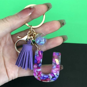 Macro shot of purple resin letter J keychain with colorful stone inlay and fringe
