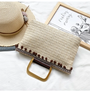 Detail of beige straw handbag with brown pom-poms and gold metal handles on a white background