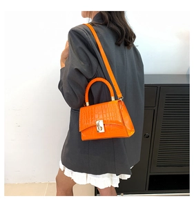Detail of orange crocodile pattern bag showing golden metal lock and woven handle