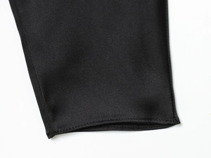 Detailed close-up of smooth black satin fabric and precise stitching on dress cuff