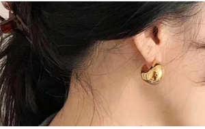 Close-up of wide 18K gold crescent hoop earrings worn on model for minimalist style