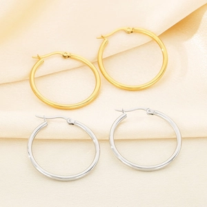 Detailed view of classic gold and silver stainless steel hoop earrings on beige fabric