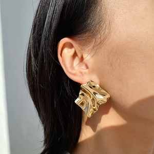 Detailed side view of large gold-finish geometric crumpled metal earrings on a model