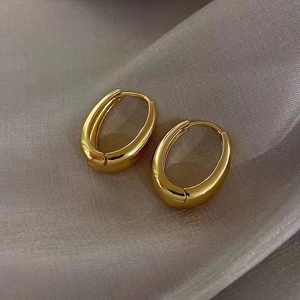 Close-up of gold oval hoop earrings with polished thick walls on grey silk fabric
