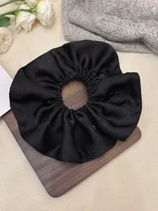 Close-up of black jacquard satin scrunchie featuring elegant 3D camellia embossed pattern