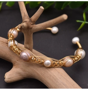 Detailed shot of handmade woven gold wire pearl bracelet on wooden branch stand