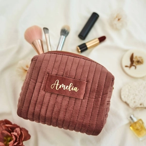 Close-up of pink corduroy makeup bag with gold Amelia embroidery on white fabric