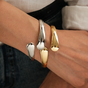 Minimalist gold and silver waterdrop open cuffs worn on wrist over white shirt